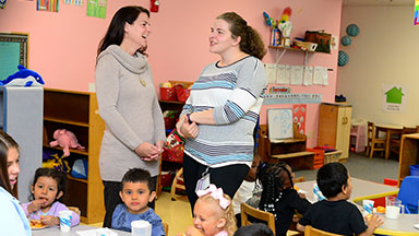 Two therapists talking with pre-school childrens playing around the them